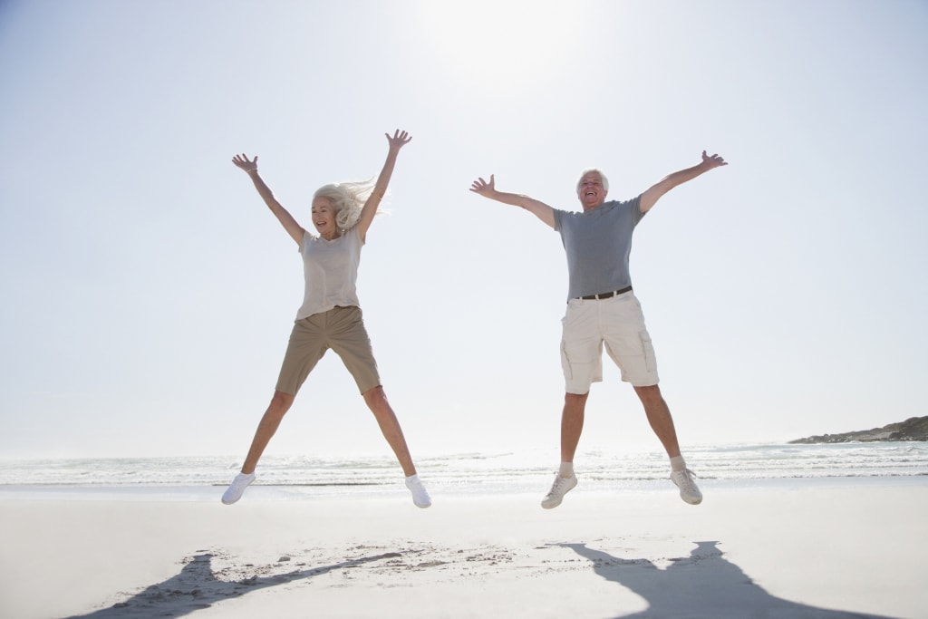 Senior couple happy with life jumping on beach